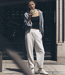 A woman in casual attire sips a green drink in front of a dark, ornate doorway.