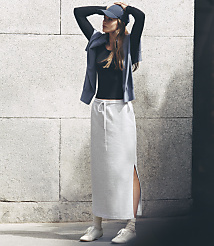 A woman in a black top, grey skirt, and blue cap stands against a textured stone wall. carousel Product Image 1