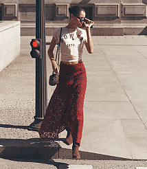 A woman in a white crop top and a long red lace skirt walks past a traffic light with a building in the background. carousel Product Image 1