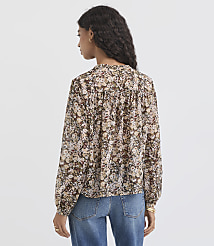 A woman in a floral blouse and jeans stands against a plain, light gray background. carousel Product Image 3