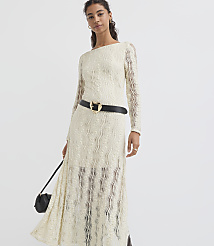 A woman in a cream-colored lace dress with a black belt and purse stands against a plain white background. carousel Product Image 2
