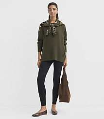 A woman in a green sweater and black leggings stands against a plain gray background, holding a brown bag. carousel Product Image 1