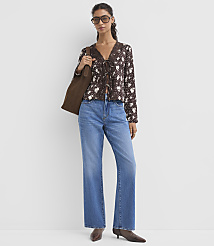 A woman in a floral blouse and jeans stands against a plain white background, carrying a brown tote bag. carousel Product Image 2