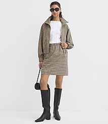 A woman in a plaid jacket and skirt stands against a plain white background, holding a black purse. carousel Product Image 1