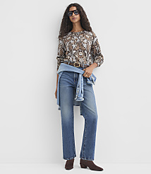 A woman in a patterned blouse and jeans stands against a plain white background, with a denim jacket tied around her waist. carousel Product Image 2