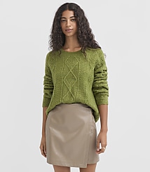 A woman in a green cable-knit sweater and a tan faux leather skirt stands against a plain gray background. carousel Product Image 2