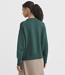 A woman in a green sweater stands against a plain, light gray background. carousel Product Image 4