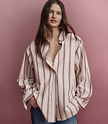 A woman in a pink and black striped oversized shirt and blue jeans stands against a plain pink background. carousel Product Image 4