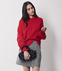 A woman in a red sweater and plaid skirt holds a studded black handbag against a plain white background. carousel Product Image 2