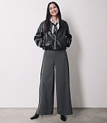 A smiling woman in a black leather jacket and pinstripe pants stands against a plain white background. carousel Product Image 4