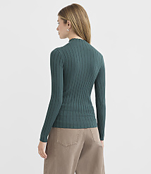 A woman in a green ribbed turtleneck and tan pants stands against a plain, light gray background. carousel Product Image 3