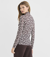 A woman in a floral blouse and brown pants stands against a plain gray background. carousel Product Image 4