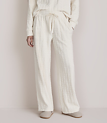 A person stands in cream-colored cable-knit pajamas and slippers against a plain, light-colored background. carousel Product Image 2