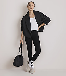A woman in a black jacket, white tank top, and black leggings stands with a black bag in her left hand against a plain white background. carousel Product Image 2