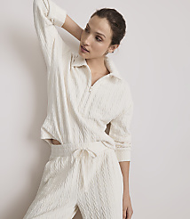 A woman in a cream-colored cable-knit loungewear set poses against a plain white background.
