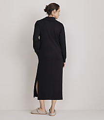 A woman in a black midi dress with side slits stands with her back to the camera, wearing light-colored slippers, against a plain, light-colored background. carousel Product Image 3
