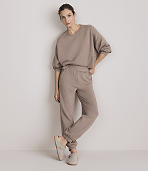 A woman in a beige loungewear set and slippers stands against a plain, light-colored wall. carousel Product Image 1