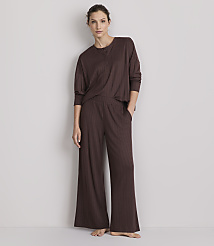 A woman in a brown ribbed pajama set stands against a plain, light-colored wall.