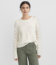 A woman in a cream cable-knit sweater and green pants stands against a plain white background. carousel Product Image 2