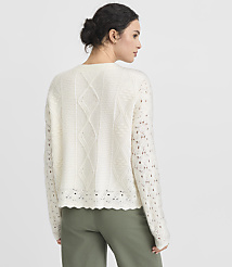 A woman in a cream-colored, cable-knit sweater and green pants stands against a plain gray background. carousel Product Image 4