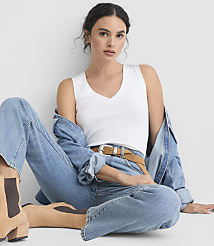A woman in a white tank top and jeans sits on a white background, with a denim jacket draped over her shoulders. carousel Product Image 1