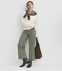 A woman in a cream sweater, olive green pants, and brown boots stands against a plain white background, holding a brown tote bag. carousel Product Image 3