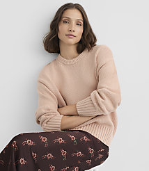 A woman in a light pink sweater and a floral skirt sits with her arms crossed against a plain white background. carousel Product Image 2