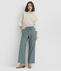 A woman in a speckled sweater vest and teal pants stands against a plain white background. carousel Product Image 1