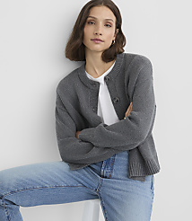A woman in a gray cardigan and jeans sits in front of a plain white background. carousel Product Image 2