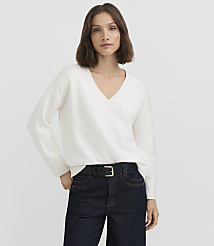A woman in a white v-neck sweater and dark jeans stands against a plain white background. carousel Product Image 1