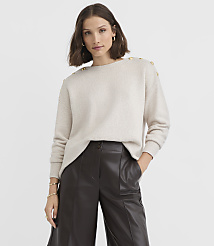 A woman in a cream sweater with gold buttons on the shoulders and dark brown leather pants stands against a plain white background. carousel Product Image 3