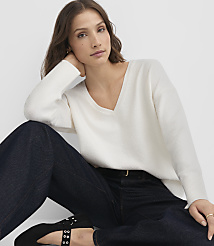 A woman in a white v-neck sweater and dark jeans poses against a plain white background. carousel Product Image 2