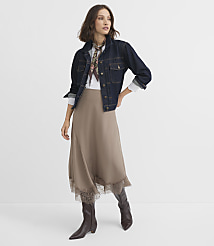 A woman in a denim jacket, white shirt, and taupe skirt with lace trim stands against a plain white background. carousel Product Image 2
