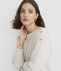 A woman in a cream-colored sweater with gold buttons on the shoulder poses against a plain gray background. carousel Product Image 2