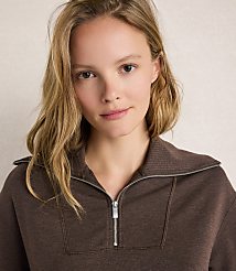 A young woman with blonde hair and a brown zippered sweatshirt is shown against a textured, light-colored background. carousel Product Image 2