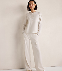 A woman in a cream-colored pajama set stands against a plain, textured wall. carousel Product Image 1