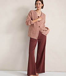A woman in a pink cardigan and maroon pants stands against a plain, textured background. carousel Product Image 1