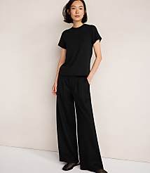 A woman in a black t-shirt and wide-leg pants stands against a plain, light-colored background. carousel Product Image 1