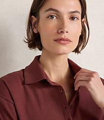 A woman with short brown hair and a maroon collared shirt is shown in the foreground, with a textured beige background behind her. carousel Product Image 3