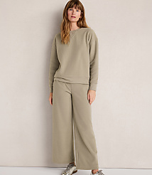 A woman in a light green sweatshirt and wide-leg pants stands against a plain, light-colored wall. carousel Product Image 2