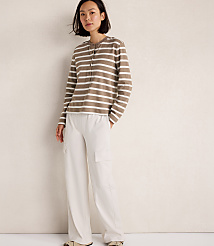 A woman in a striped long-sleeve shirt and white cargo pants stands against a textured cream wall. carousel Product Image 2