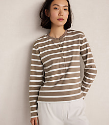 A young woman in a striped long-sleeved shirt stands against a plain, textured wall. carousel Product Image 1