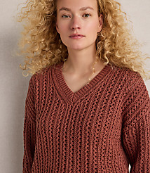 A young woman with curly blonde hair wears a rust-colored v-neck sweater in the foreground, against a plain, light-colored background. carousel Product Image 2