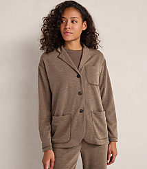 A woman with curly brown hair stands in the foreground wearing a brown blazer over a brown t-shirt and matching pants, against a plain, light-colored background. carousel Product Image 1