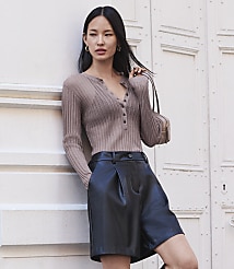 A woman in a brown ribbed top and black leather shorts leans against a white door. carousel Product Image 4