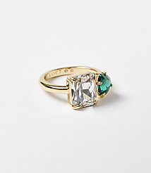 A gold ring with a rectangular clear stone and a heart-shaped green stone sits on a plain white background. carousel Product Image 1