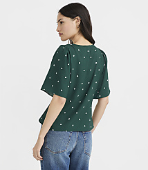 A woman in a green polka dot blouse and blue jeans stands against a plain white background. carousel Product Image 3