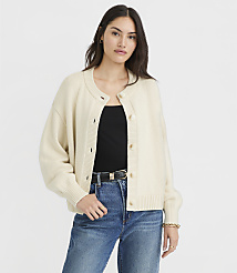 A woman in a cream cardigan and blue jeans stands against a plain white background. carousel Product Image 1