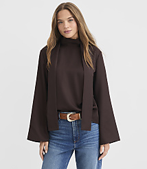 A woman in a brown mock-neck top with wide sleeves and blue jeans stands against a plain white background. carousel Product Image 1