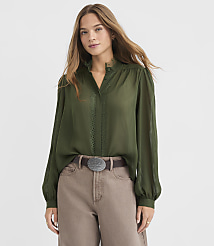 A woman in a green blouse and brown pants stands against a plain gray background. carousel Product Image 2